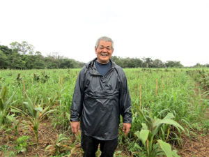 新規の畑を背に泉延吉副会長(徳之島コーヒー生産者会)