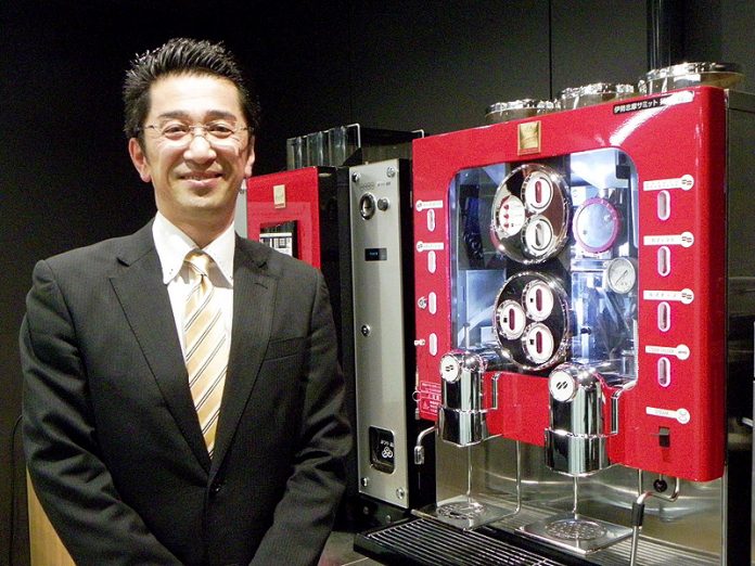 アペックスがオフィス向けに売り込んでいるカフェサーバーシステム「M-one Cafe′ Coffee System」の中核となるレギュラーコーヒー・エスプレッソ抽出兼用マシン「ＣＳ－１」と取材に応じた田口事業統括本部ＣＳ事業本部副本部長