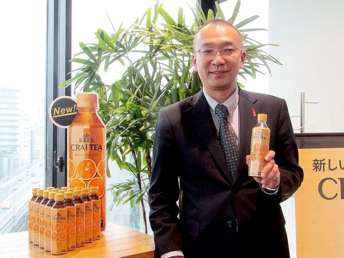 「紅茶花伝　クラフティー　贅沢しぼりオレンジティー」を手に山腰欣吾グループマネジャー