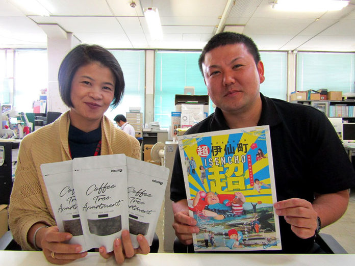 （左から）「珈琲葉茶」など返礼品をアピールする松岡由紀主査と移住・定住ガイドブックを持つ嘉納寿成主事（伊仙町）
