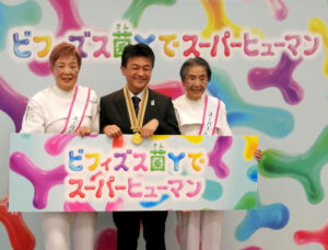 森永乳業の湯谷万博推進局長㊥とスーパーシニアアテンダントの松村好子さん㊧半田百合子さん写真大 「森永乳業の湯谷万博推進局長㊥とスーパーシニアアテンダントの松村好子さん㊧、半田百合子さん」