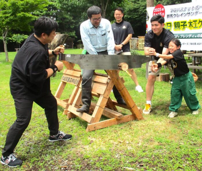 丸太切り体験の様子。子どもをサポートする細川一輝選手（右から2番目）見守る池田親平アシスタントコーチ兼スキルコーチ（中央奥）、丸太に乗って丸太を安定させる赤城南麓森林組合の石塚征人理事兼事業部部長