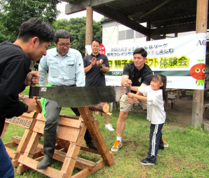 丸太切り体験の様子。子どもをサポートする細川一輝選手（右から2番目）見守る池田親平アシスタントコーチ兼スキルコーチ（中央奥）、丸太に乗って丸太を安定させる赤城南麓森林組合の石塚征人理事兼事業部部長