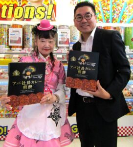 左から「アパ社長カレー煎餅 4枚入箱」をアピールするアパホテルの元谷芙美子社長と三州製菓の斉之平一隆社長