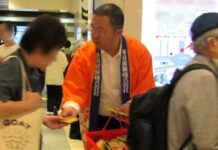 「亀田の柿の種」ビールに合うおつまみから領域拡大 「うましお」でおやつ需要を獲得 髙木社長COOがブランド磨きに自信 10日、東京駅一番街地下1階ののぞみ広場で道行く人に「亀田の柿の種 うましお」の試食品を手渡す亀田製菓の髙木社長COO