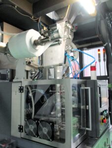 ミルとけ製造工程②充填エリアの下層階の充填機2本のパイプ上部から原料が投下される 「ミルとけ」製造工程②充填エリアの下層階の充填機。2本のパイプ(上部)から原料が投下される。