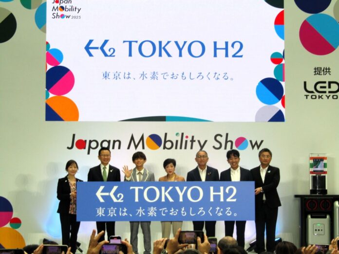 左から松本明子東京都副知事、JR東日本の松本雄一執行役員グループ経営戦略本部経営企画部門長、松丸亮吾さん、小池百合子都知事、SEJの山口繁執行役員、UCCジャパンの里見陵執行役員、トヨタの山形光正水素ファクトリープレジデント