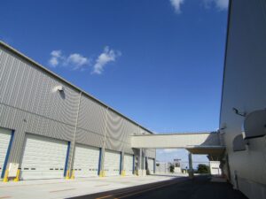 コンベアで結ばれる湖池屋中部工場右とトランコムの物流倉庫左 コンベアで結ばれる湖池屋中部工場(右)とトランコムの物流倉庫(左)