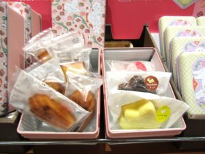 「お菓子クラブ缶」に詰められた「ガトー・ド・ボワイヤージュ バラ菓子」（左）と「AKI プレミアムもみじ1個」（右）