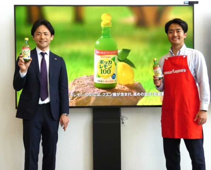 「ポッカレモン100」のTVCMを背景にマーケティング本部ブランドマネジメント部宣伝販促グループの肥後亮グループリーダー（左）と営業本部首都圏営業本部東京支社の廣田一航さん