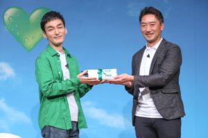 草彅剛さんにオリジナルの折りたたみ日傘をプレゼントする皆福（かいふく）哲哉ブランドマーケティング本部部長（右）