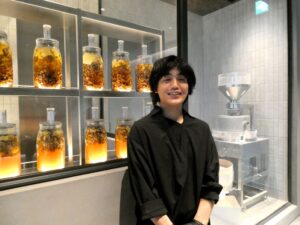 ベーカリー店舗「PAN：013」のブーランジェ木村勇一さん。石臼（右奥）とショーケースに並ぶ四季折々の自家製酵母