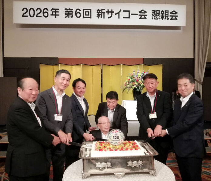 車椅子からケーキカットする石光輝男名誉会長㊥、荒川正臣社長（左から3人目）と、取引先代表者