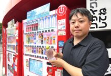 コカ・コーラ自販機にラベルレスボトル初導入 キャップに全ての表示項目を表記して新境地開拓 「い・ろ・は・す 天然水」で始動 日本コカ・コーラ本社前の自販機でデモンストレーションした日本コカ・コーラの大島遊ベンディング事業本部ベンディングRGMXシニアマネジャー
