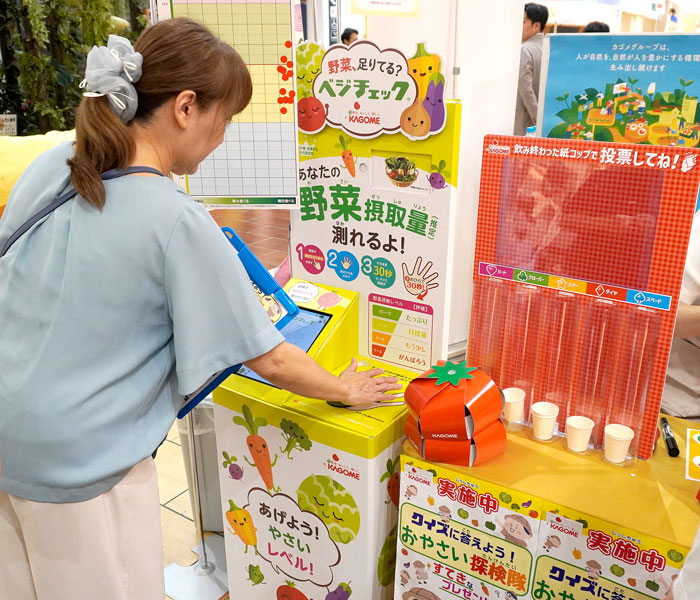 カゴメブースの「ベジチェック」で野菜摂取量を計る主婦